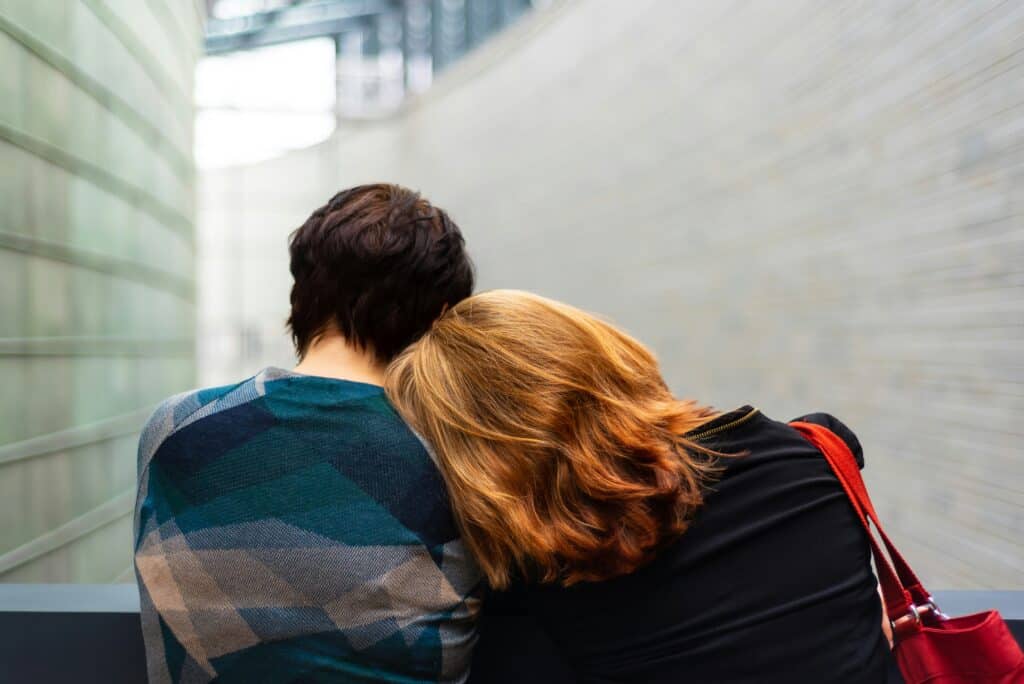A husband and wife lean against each other on a bench.