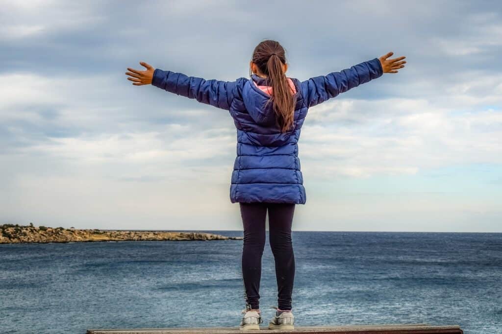 Girl raising arms in front of the ocean