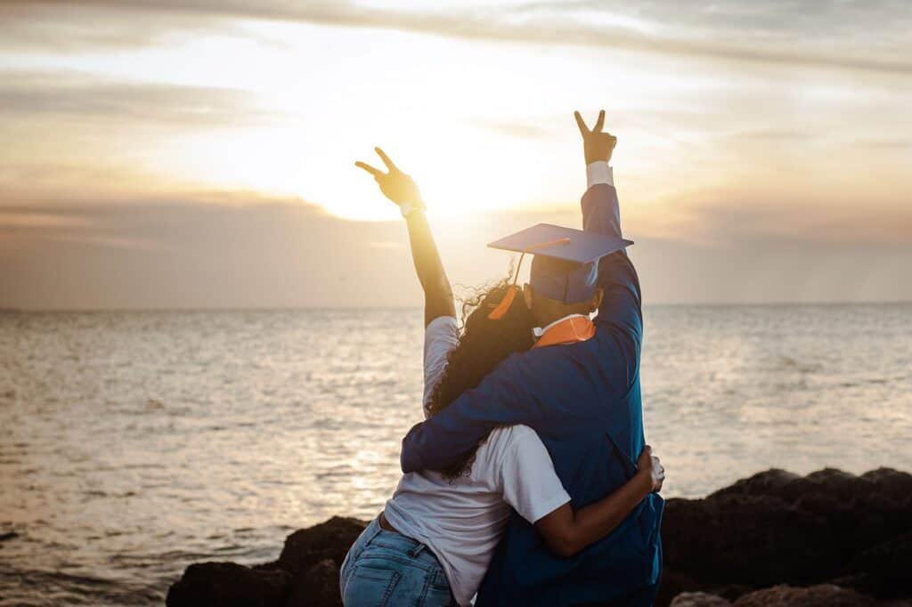 male graduate and girl cheering near ocean