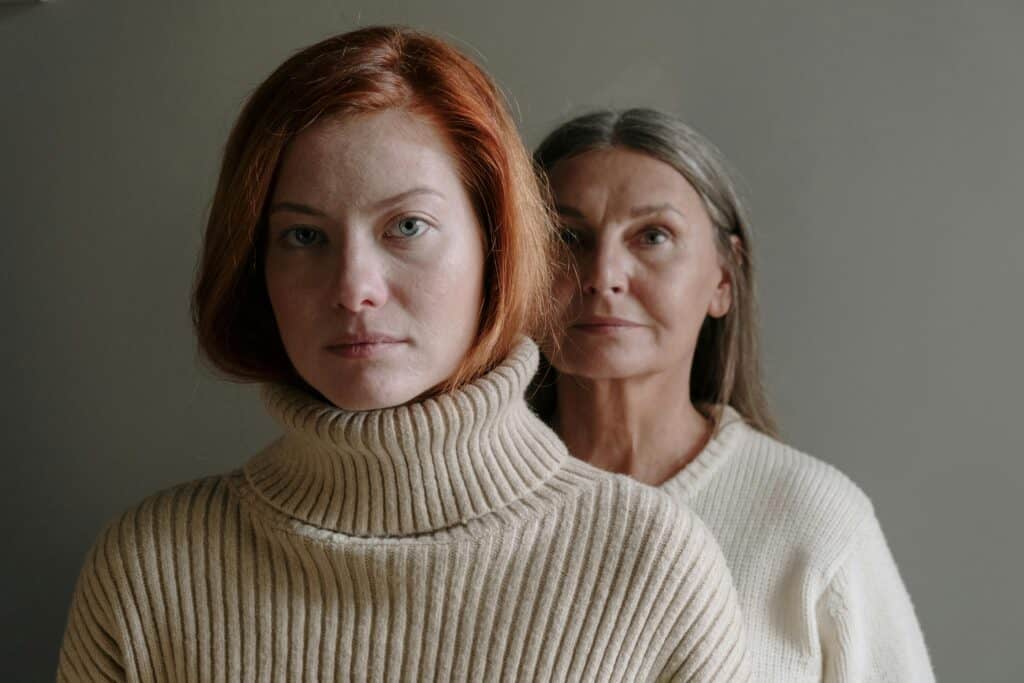 mom standing behind adult daughter both serious