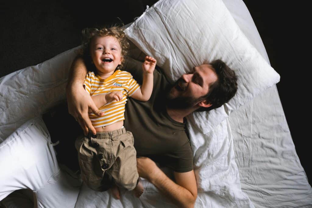 man lying on bed laughing with preschool boy