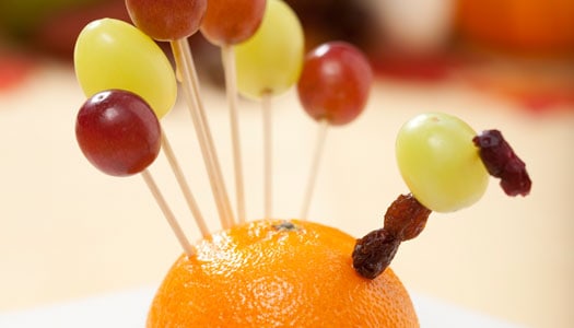 Close up of an orange creatively decorated to look like a turkey using toothpicks and grapes to form feathers