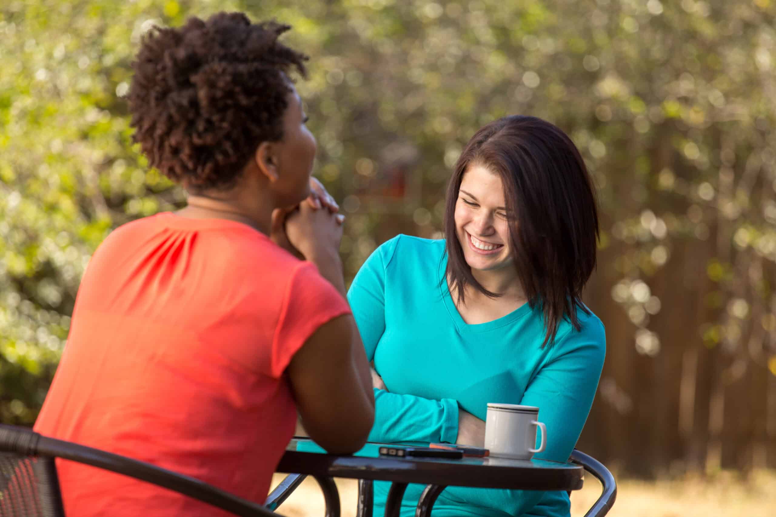 Two women sitting at an outdoor table and talking.